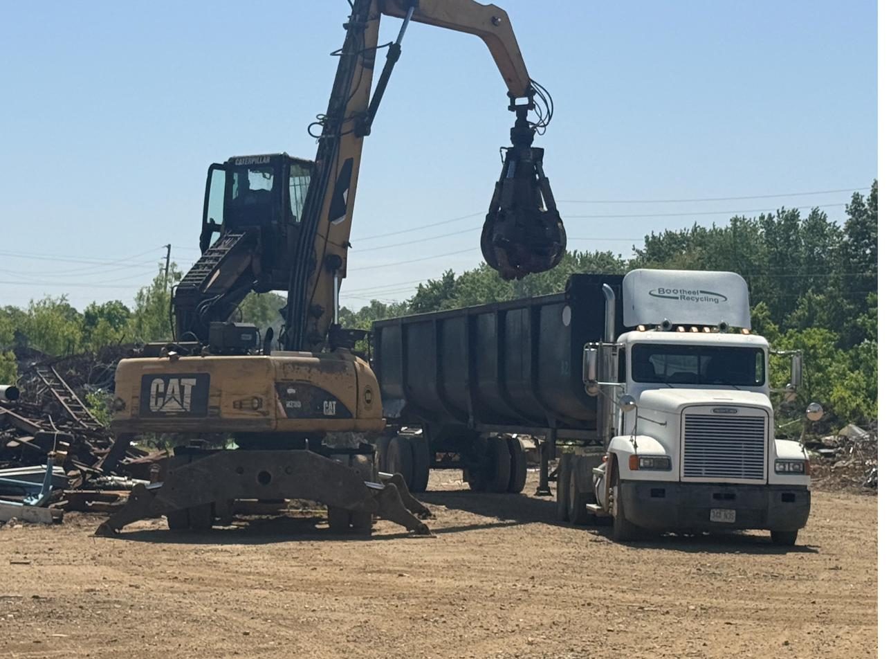 Material handler loading recyclable scrap into a roll-off trailer — recovered through affiliated operations
